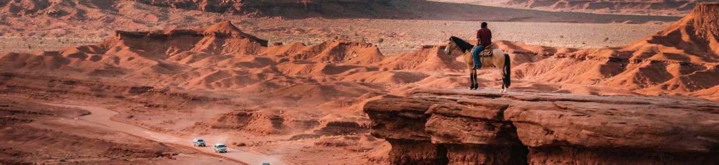 Dine tribal member on horseback looking out over red sandstone dunes navajo nation