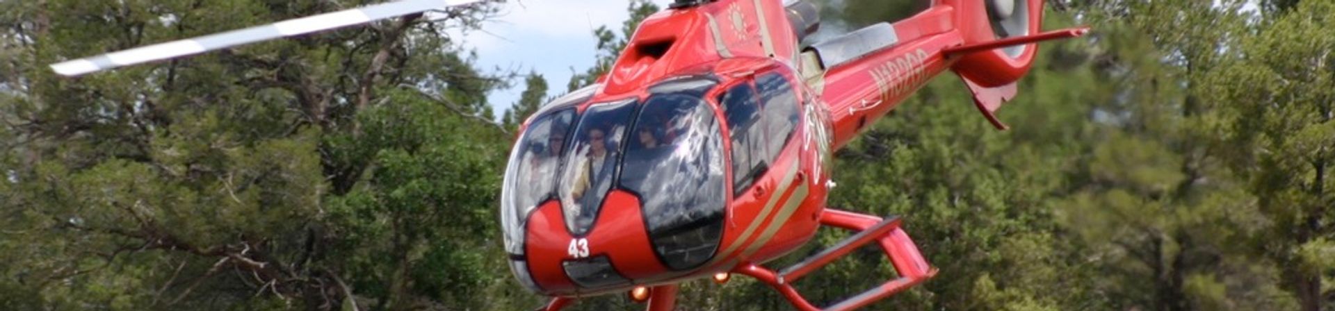 A Grand Canyon Tour Helicopter Red Eurocopter EC130 B4 taking off with forest in background